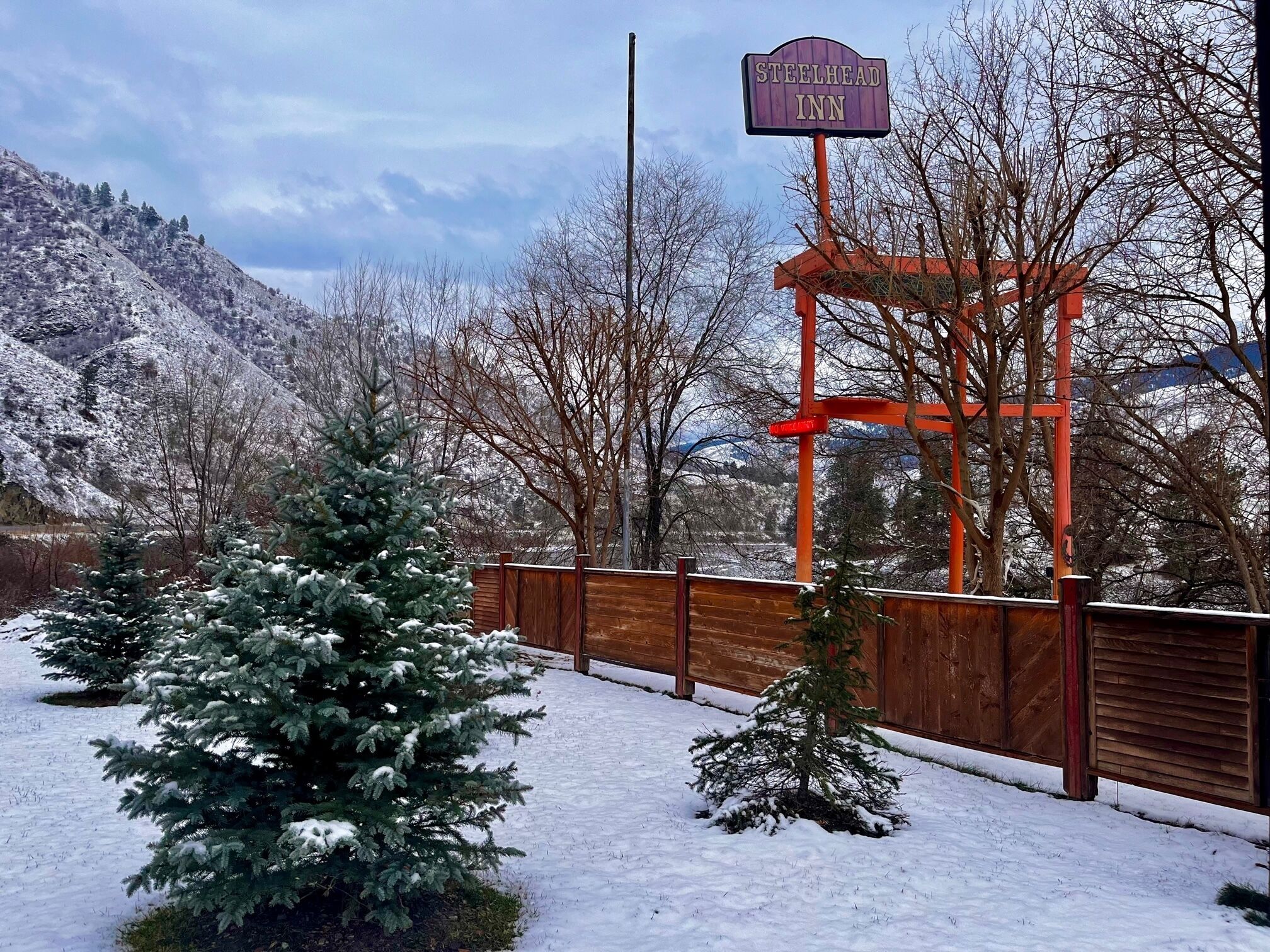 Een bordje voor Steelhead Inn, met een houten hek en sneeuwbedekte bomen op de achtergrond.