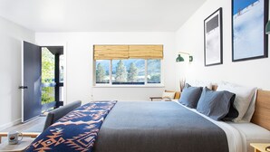 A modern bedroom with a large bed, a desk, and a window with a view of trees. - Steelhead Lodge (Lucile)