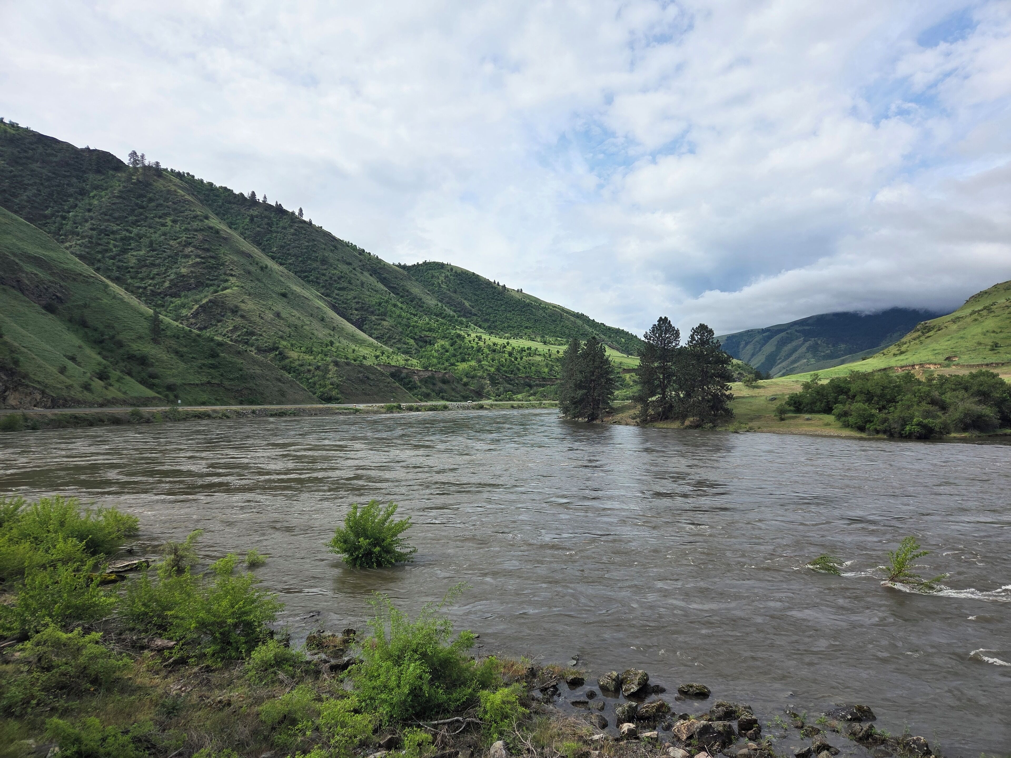 Une rivière qui traverse une vallée, bordée de collines verdoyantes et d’arbres.