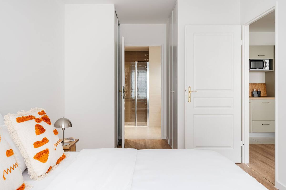 Een hotelkamer met een bed, een nachtkastje, een lamp, een badkamer met douche en een kitchenette met een magnetron.