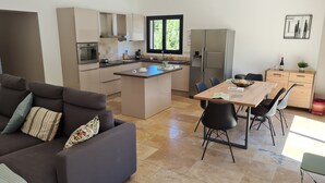 A modern kitchen with a central island, a dining area with a wooden table and chairs, and a living area with a sofa and cushions. - Recent villa with air conditioning and private pool on the heights of Barjac (Barjac)