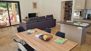 A modern living room with a sofa, a dining table with chairs, a kitchen area, and a view of the outdoors. - Recent villa with air conditioning and private pool on the heights of Barjac (Barjac)