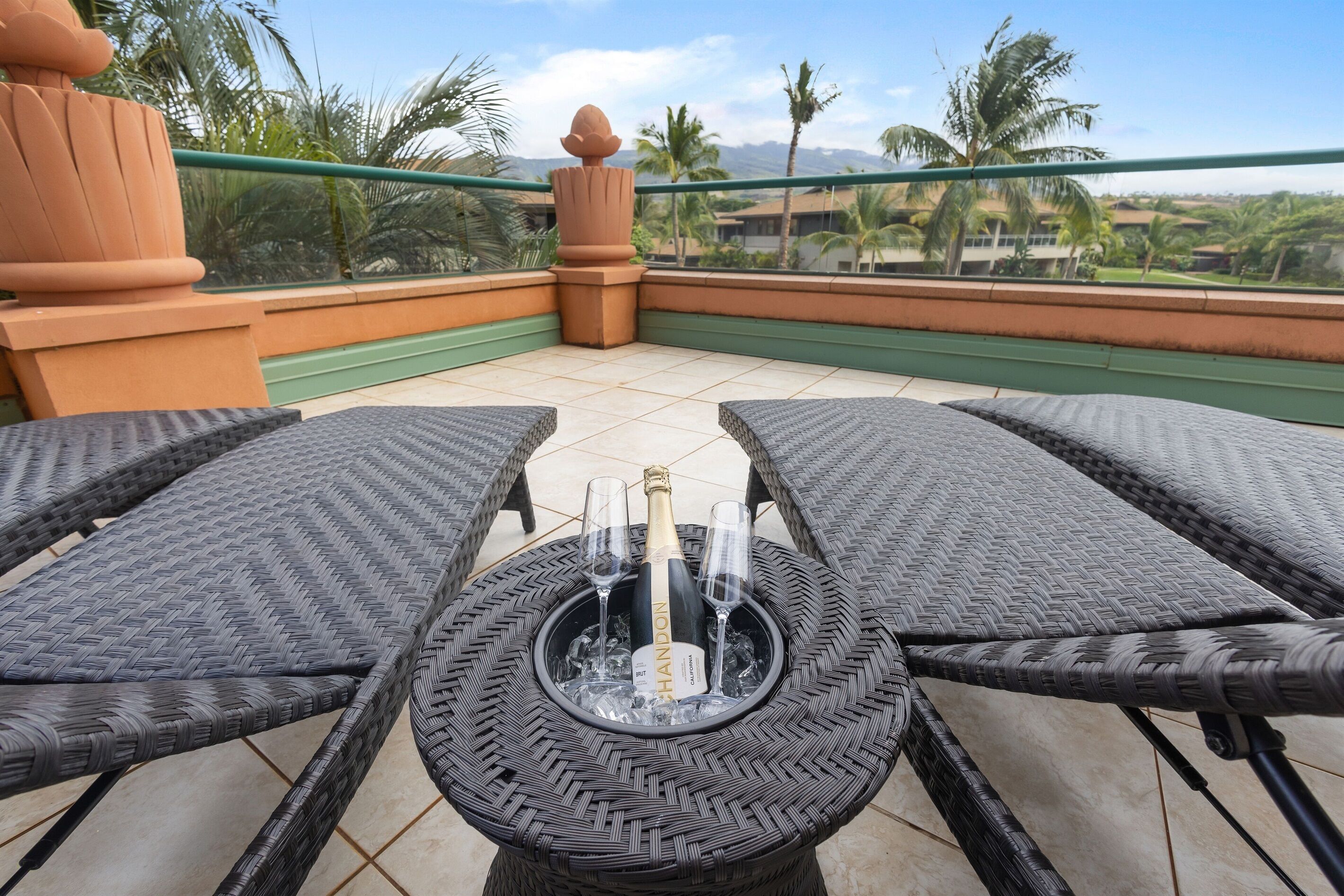 A balcony with wicker furniture, a bottle of champagne, and glasses.