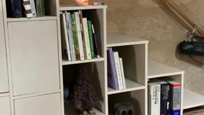 Uma estante branca com livros, uma vela e objetos decorativos.