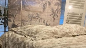 Uma cama com colcha estampada com flores em quarto com piso de madeira e painel decorado com tema tropical.