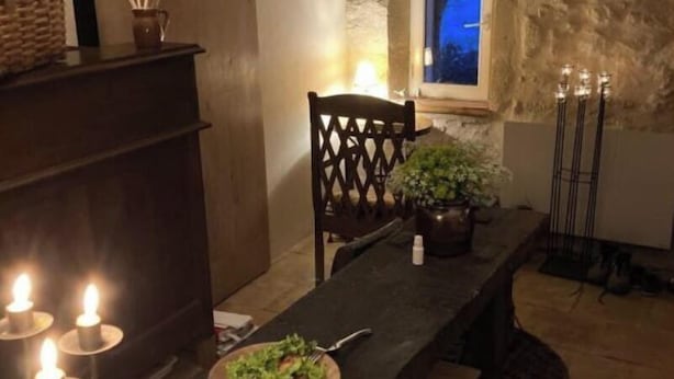 Uma área de jantar com mesa de madeira, velas e vista para o exterior através de uma janela.