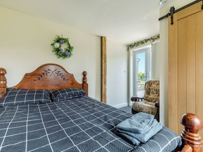 A bedroom with a wooden headboard, a checkered bedspread, a blue blanket, a wooden chair, and a sliding door leading to an outdoor area. - Greystones Nawab Annex C (Flagg, Buxton)