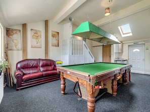 A pool table in a room with a red leather sofa, a staircase, and a door with an exit sign.
