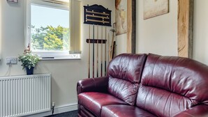 Une pièce avec un canapé en cuir rouge, une fenêtre donnant sur des arbres, un radiateur et une horloge murale.