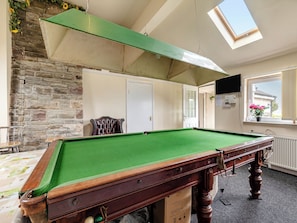 A pool table in a room with a stone wall, a window with a view, and a ceiling light fixture.