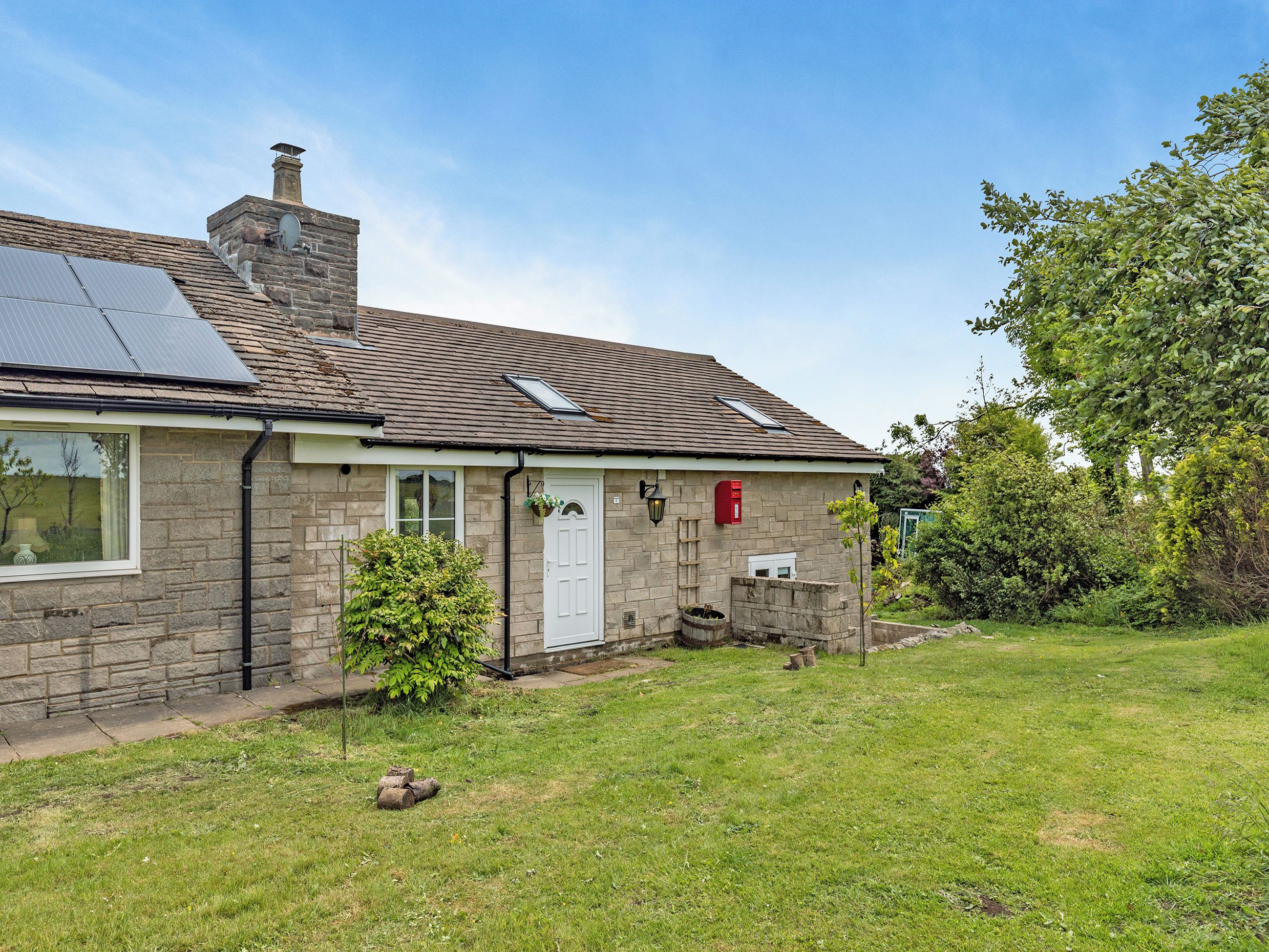 Une maison en pierre avec un panneau solaire, une porte blanche et une boîte aux lettres.