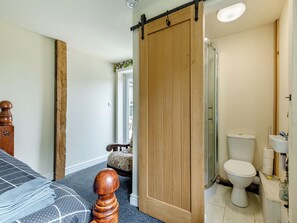 A bedroom with a bed, a wooden wardrobe, a sliding door, a bathroom with a toilet, and a shower. - Greystones Nawab Annex C (Flagg, Buxton)
