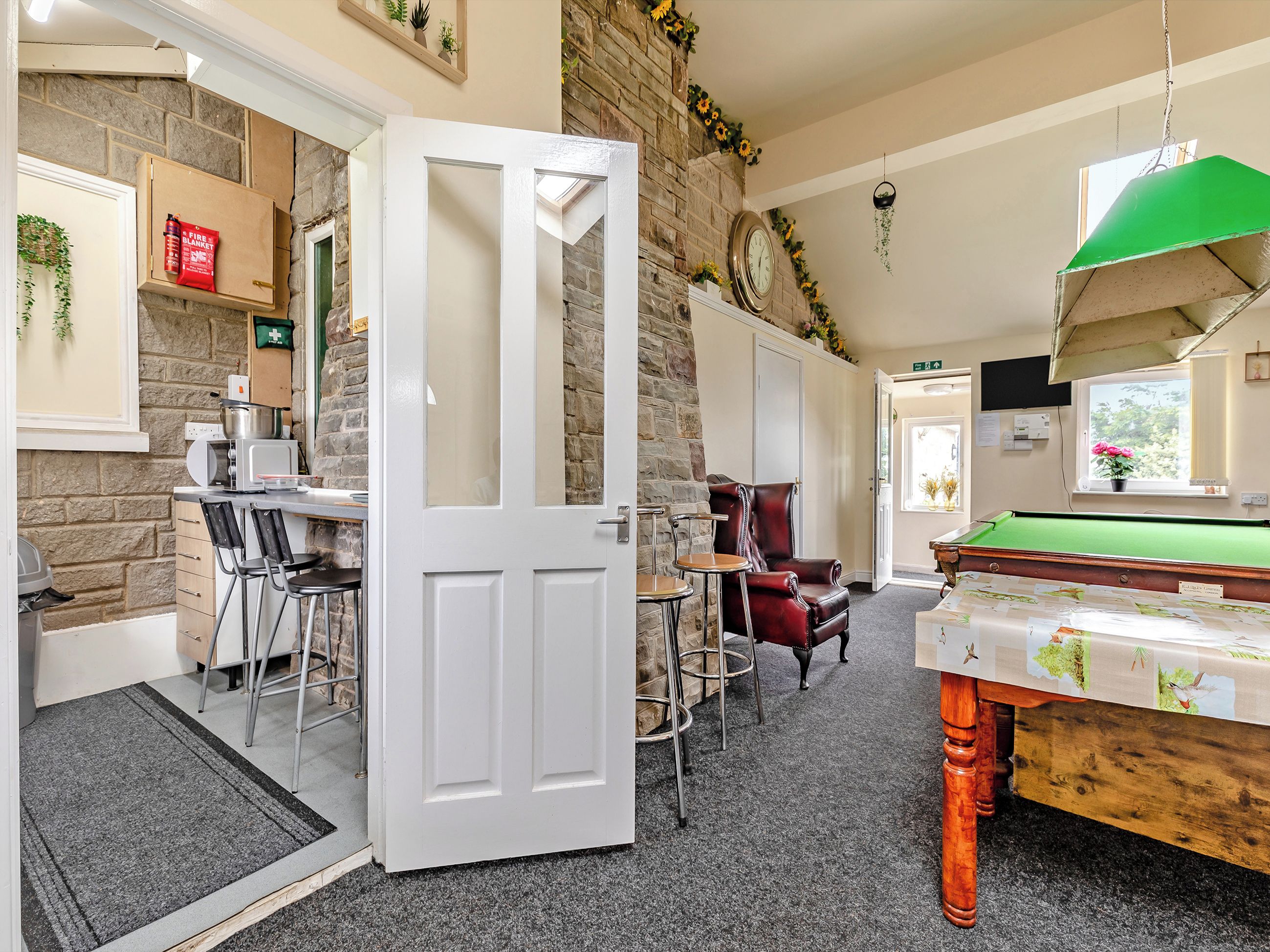 Une pièce chaleureuse avec une table de billard, un fauteuil en cuir rouge et une porte blanche donnant sur un autre espace.