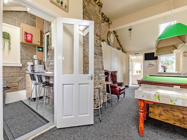 A cozy room with a billiards table, a red leather chair, and a white door leading to another area.