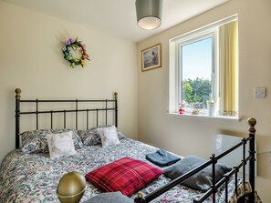 A bedroom with a bed, a window with curtains, a wall-mounted picture, and a decorative wreath. - Greystones Nawab Annex C (Flagg, Buxton)