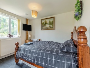A bedroom with a bed, a television, a painting, and a window with curtains.