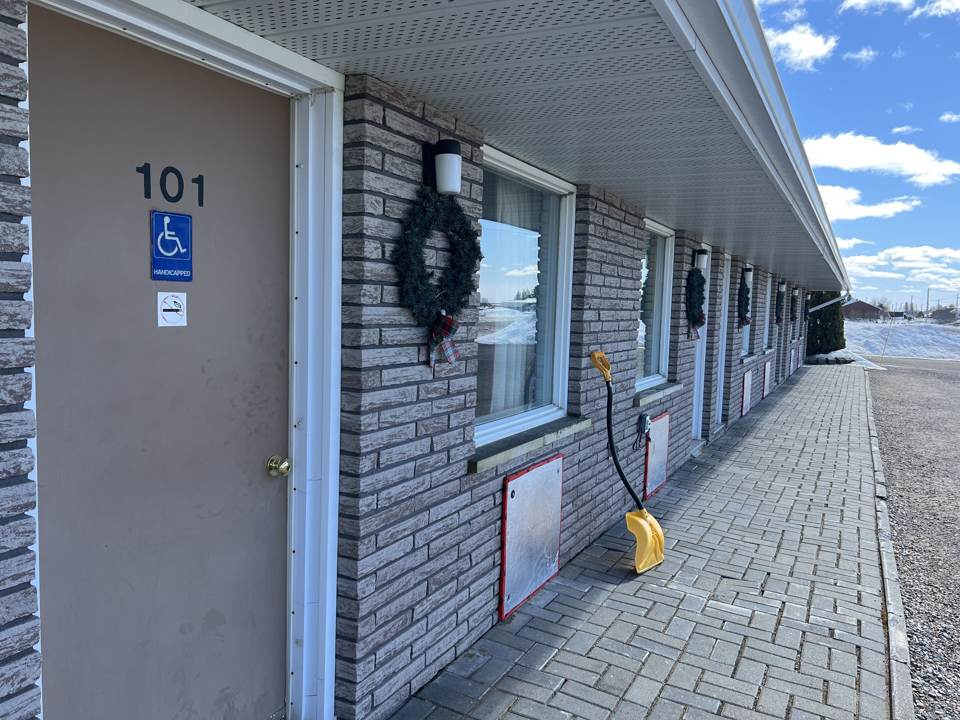 Un edificio de fachada de ladrillo, número 101, con entrada accesible para personas con discapacidad, ventanas decoradas con coronas y un camino pavimentado.