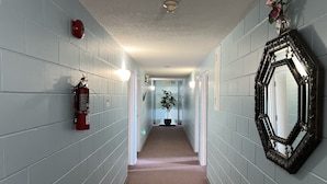 Un couloir aux murs bleu clair, avec un extincteur, une plante en pot et un miroir.