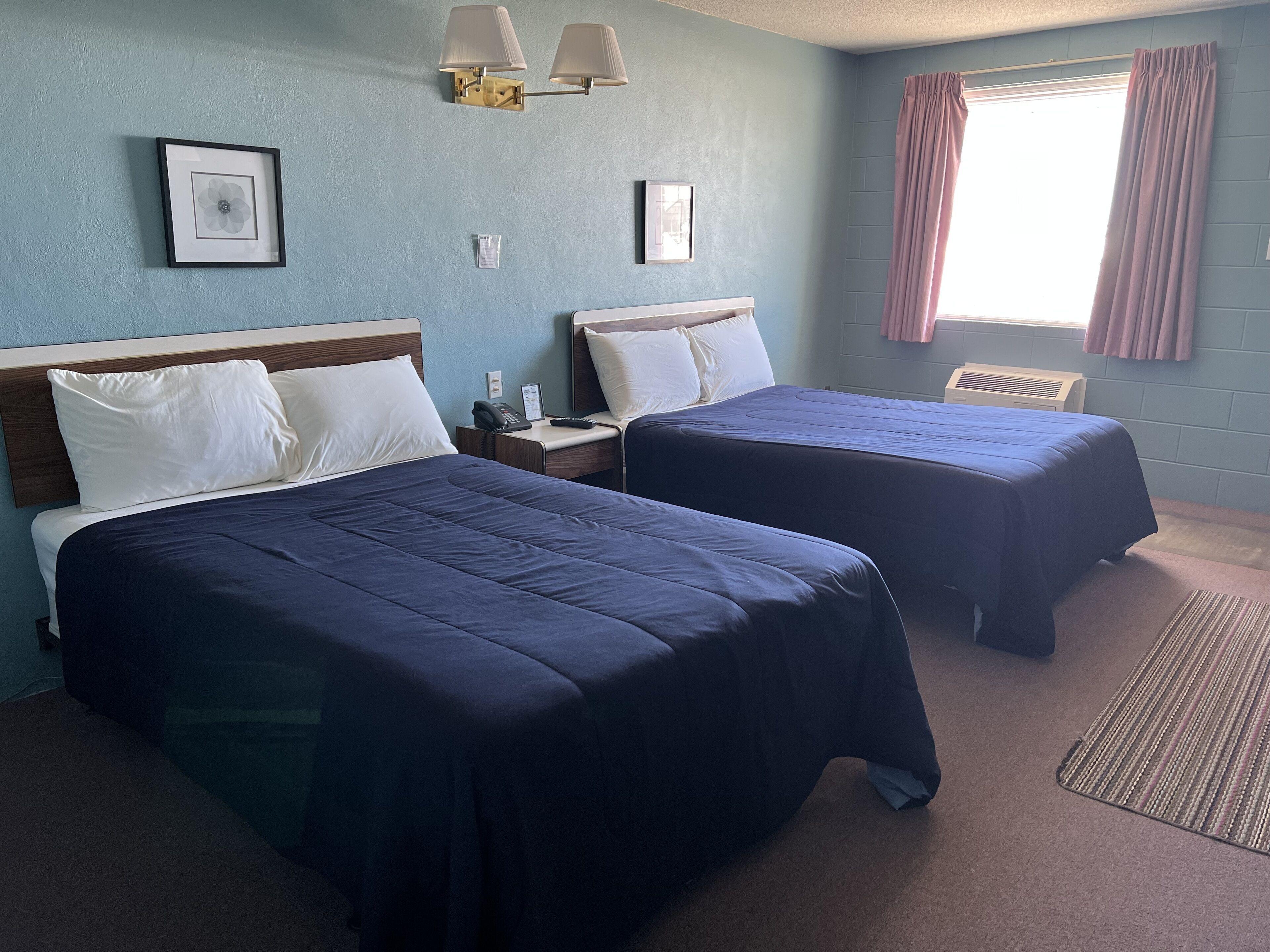 A hotel room with two beds, a nightstand, a phone, and a window with curtains.