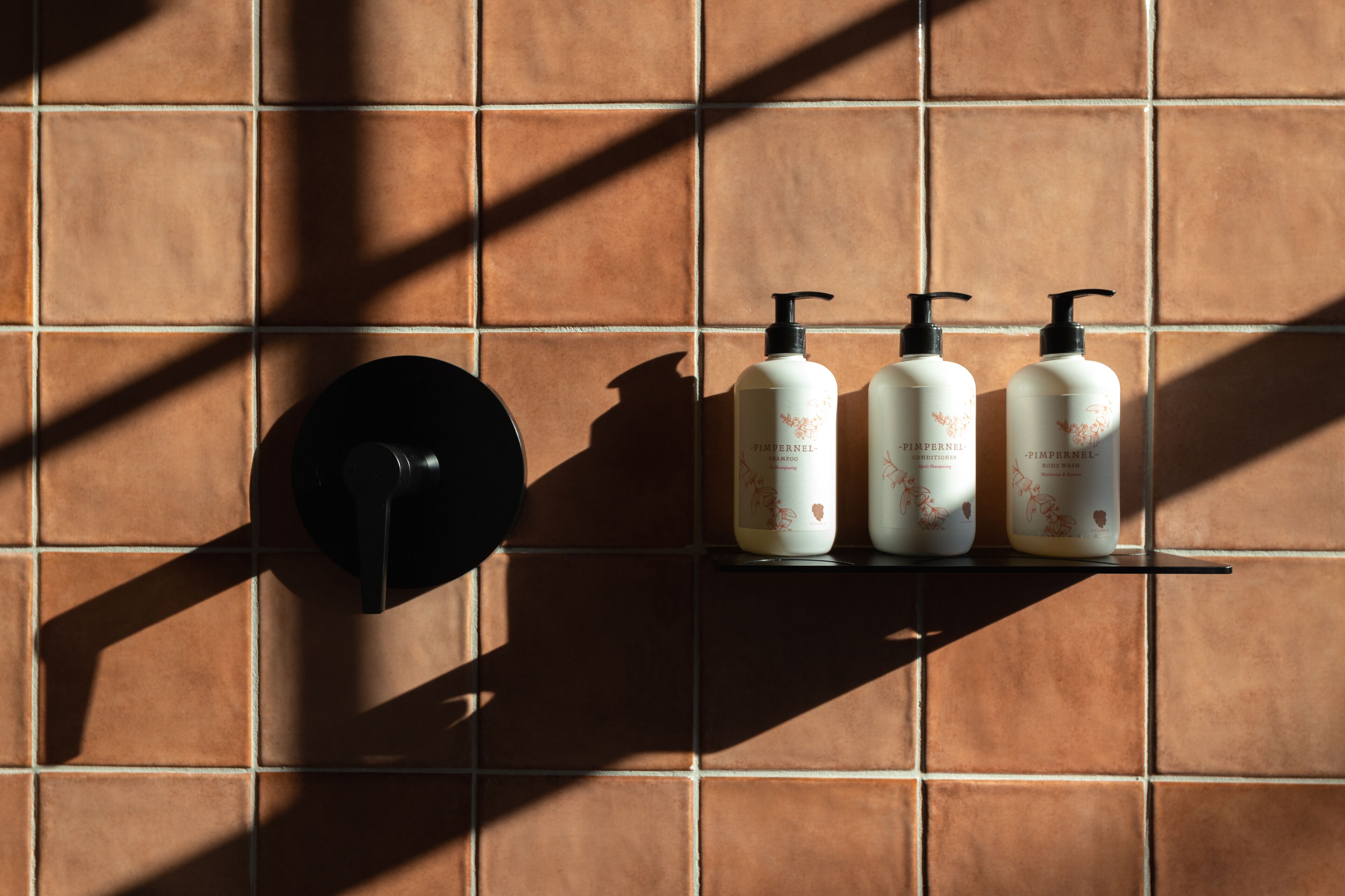 A bathroom with a black faucet and three bottles of Dove body wash on a shelf against a tiled wall.