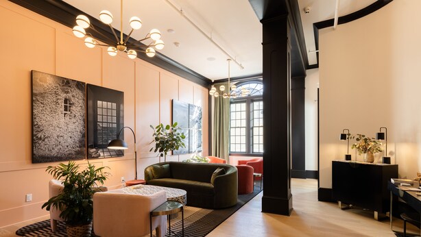 A modern living room with a sofa, coffee table, and potted plants. There is a dining area with a table and chairs. The room has large windows and a chandelier. - Hotel Thaxter (Portsmouth)