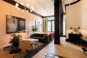 A modern living room with a sofa, coffee table, and potted plants. There is a dining area with a table and chairs. The room has large windows and a chandelier. - Hotel Thaxter (Portsmouth)
