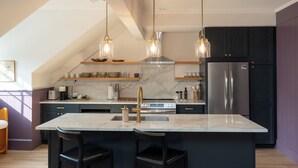 A modern kitchen with a central island, stainless steel appliances, and pendant lighting. - Hotel Thaxter (Portsmouth)