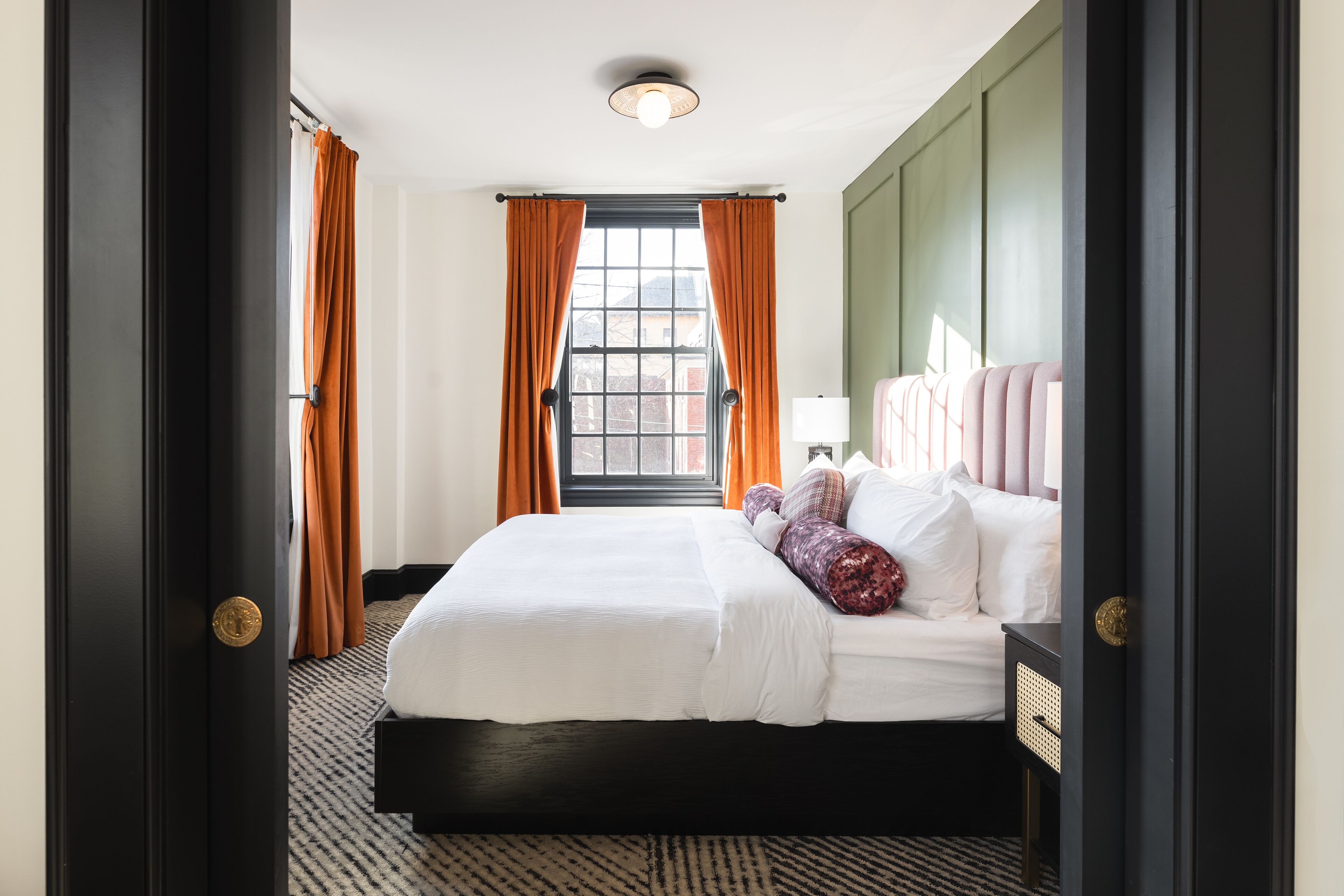 A hotel room with a large bed, a nightstand, a window with curtains, and a headboard.