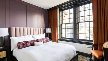A hotel room with a large bed, a nightstand with a lamp, a chair, and a window with curtains.