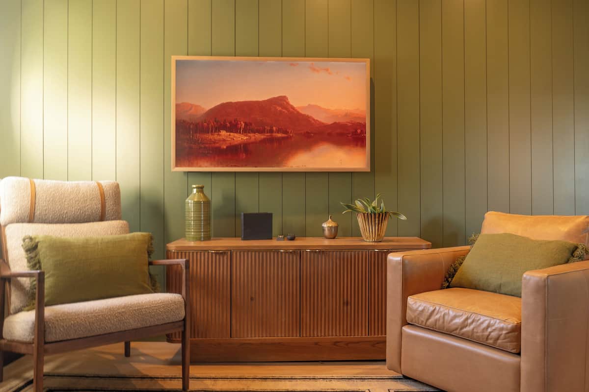 Une pièce comprenant deux fauteuils en cuir, un meuble en bois et un tableau représentant un paysage, accroché au mur.