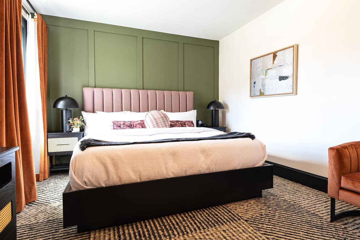 Une chambre d’hôtel moderne avec un grand lit, une tête de lit, deux tables de chevet avec des lampes, une chaise et un tableau au mur.