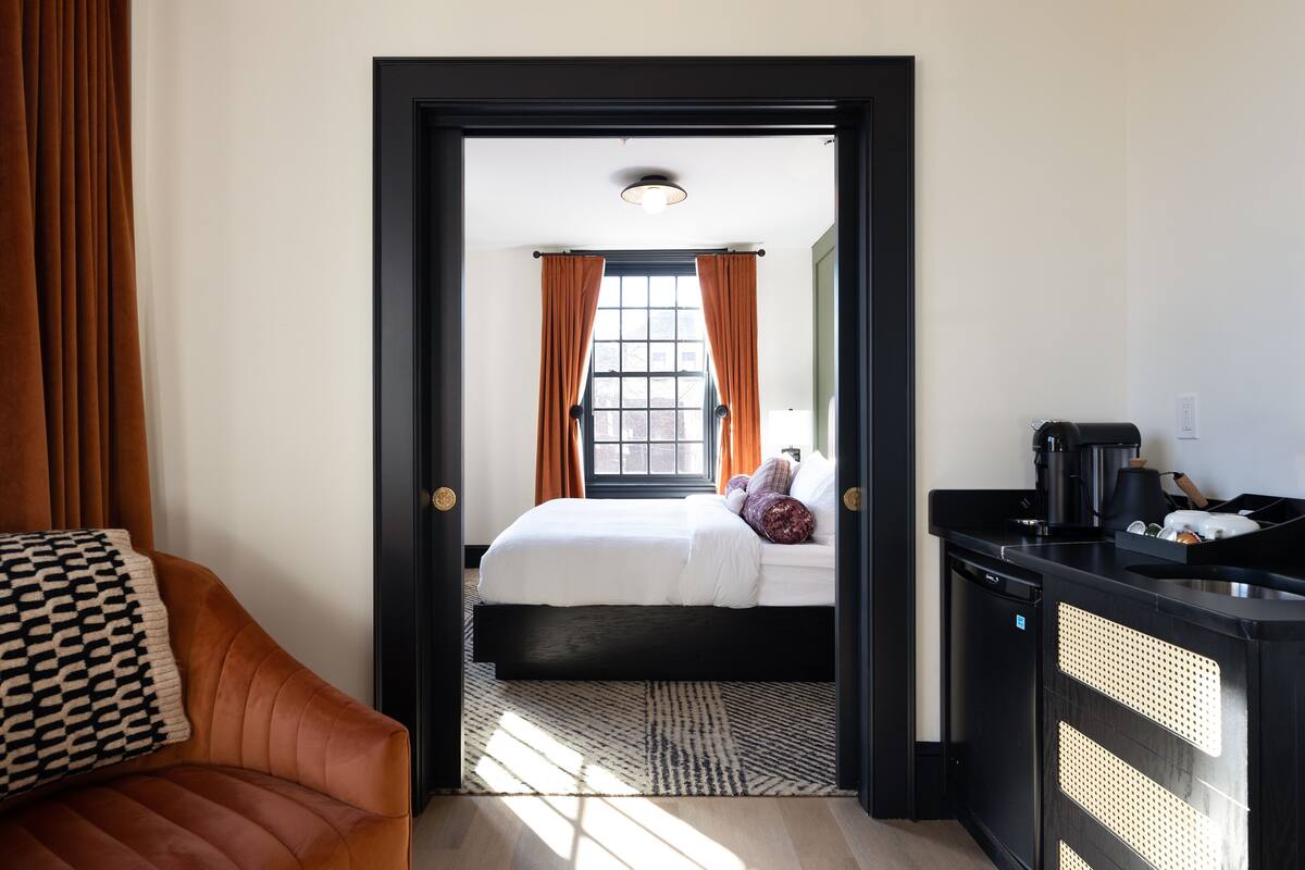 Une chambre d’hôtel avec un lit, un bureau doté d’une machine à café et une vue sur l’extérieur par une fenêtre munie de rideaux.