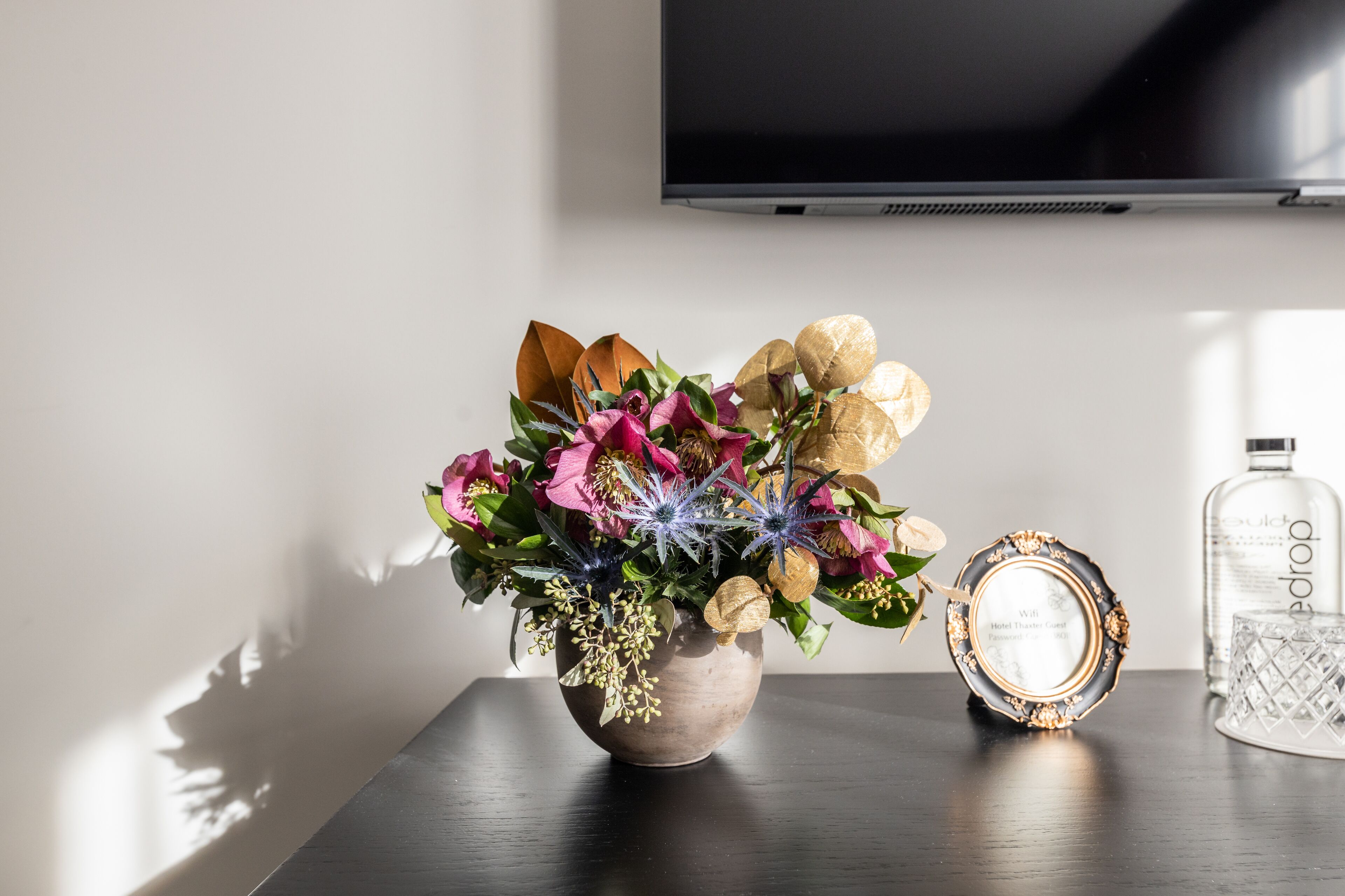 A floral arrangement in a vase on a table, a decorative frame, and a bottle of alcohol.