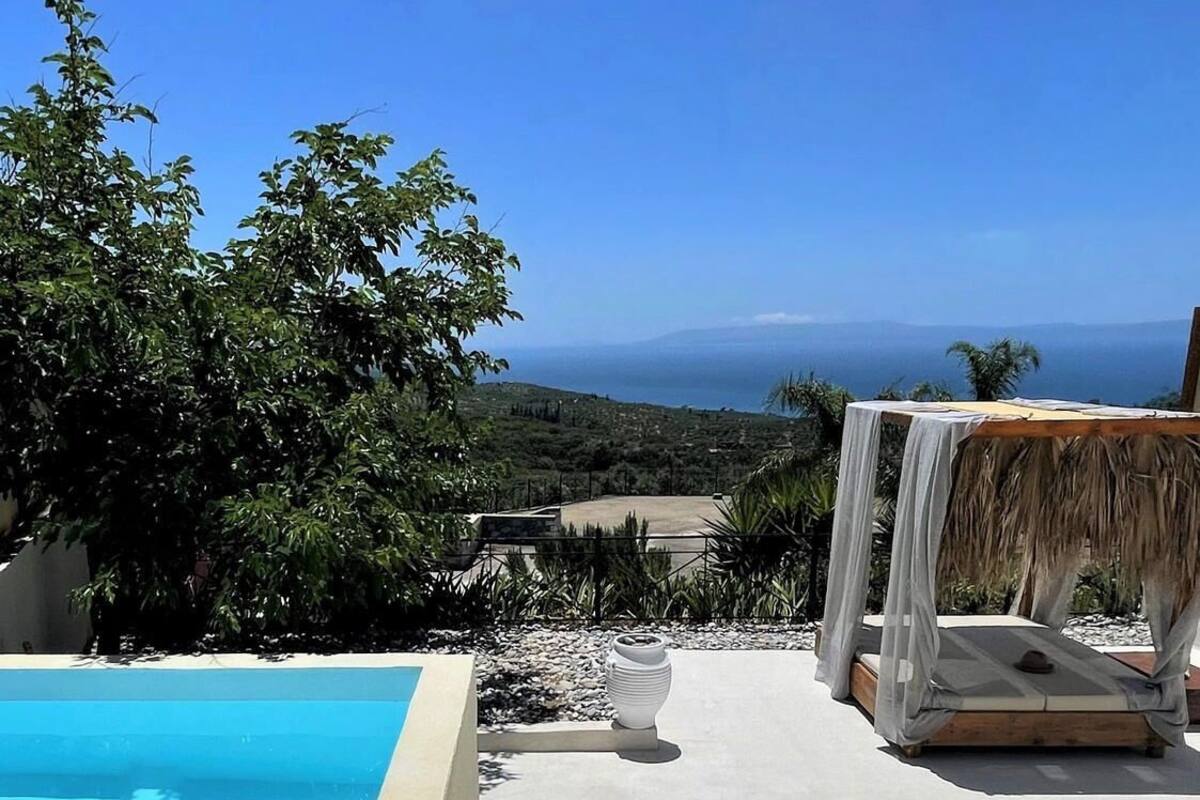 Zona de piscina con vista despejada al mar y colinas al fondo.