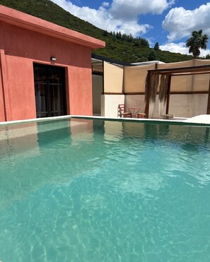 A clear pool with a red building and a covered seating area. - Rustic Hill Private Pool Rooms (Kalamata)
