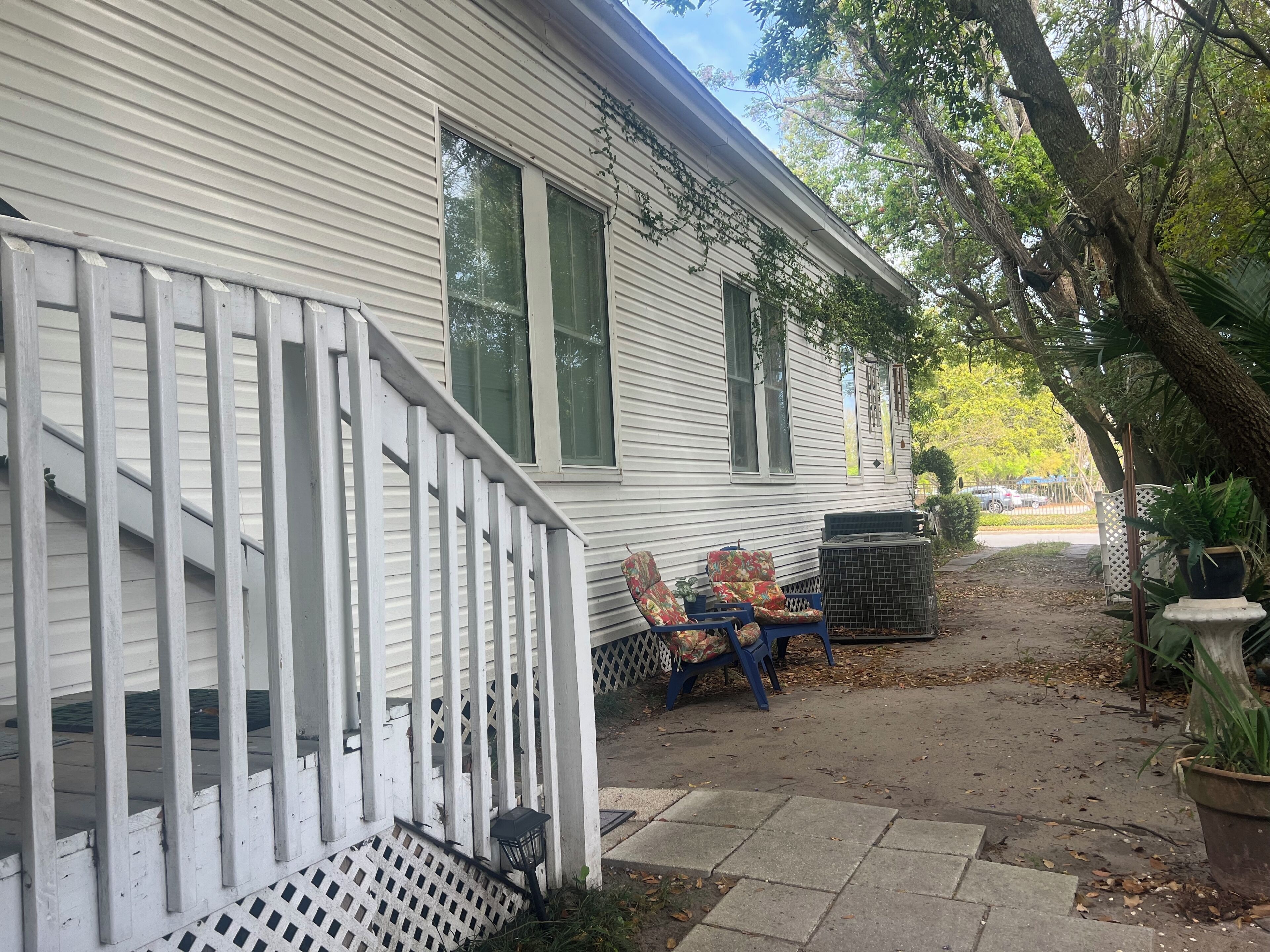 A white house with a porch, two chairs, a trash can, and a potted plant.
