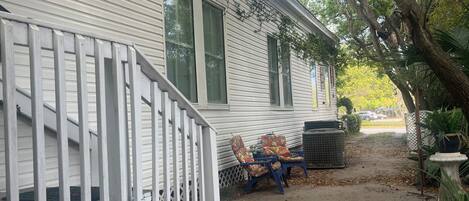 A white house with a porch, two chairs, a trash can, and a potted plant.