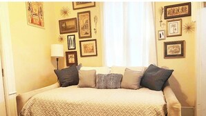 Un dormitorio con una cama grande, varias almohadas, una lámpara de noche y cuadros en la pared.