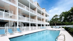 A swimming pool with a white deck, lounge chairs, and a multi-story building with balconies. - Spacious 7 BD walk to the beach + pool (North Myrtle Beach)
