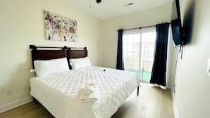 A hotel room with a large bed, a flat-screen TV mounted on the wall, and a window with curtains. - Spacious 7 BD walk to the beach + pool (North Myrtle Beach)