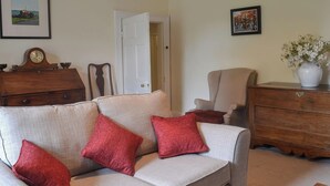 A living room with a sofa, red cushions, a wooden dresser, a chair, and a clock.
