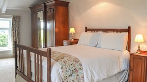 A neatly made bed with a floral bedspread, two bedside lamps, a wooden wardrobe, and a hanging lamp.