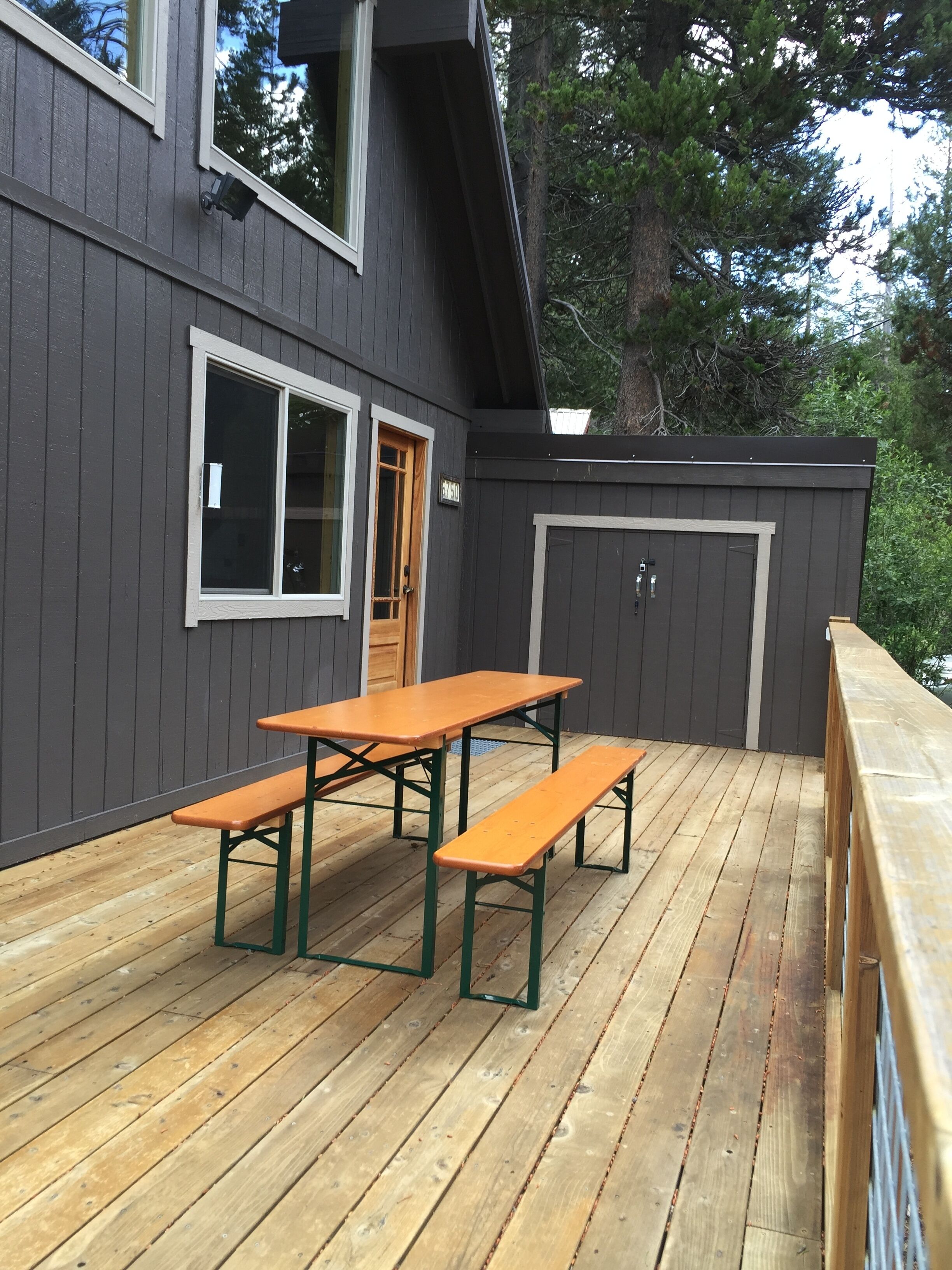 A deck with picnic tables and a door, surrounded by a dark wooden fence.