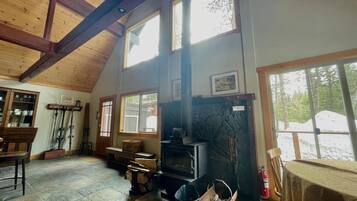 A cozy room with a fireplace, wooden beams, and large windows.