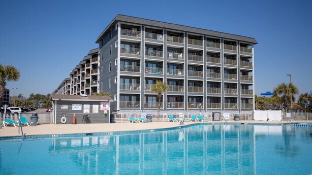 Ein mehrstöckiges Hotel mit Schwimmbad, Balkonen und einer Rettungsschwimmerstation.