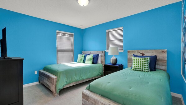 A bedroom with two beds, each with a wooden headboard, a nightstand, a lamp, and a window with blinds.