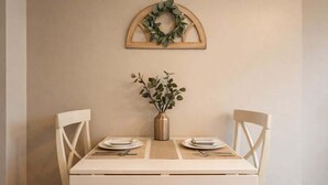 A dining table with two chairs, a vase with greenery, and a wooden wreath on the wall.