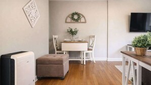 A modern living room with a dining area, a flat-screen TV mounted on the wall, and a small table with a potted plant.