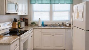 A kitchen with white cabinets, a stove, a sink, and a refrigerator.