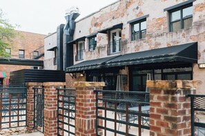 Un bâtiment à la façade en briques, doté d’un auvent noir et d’un espace extérieur aménagé avec des tables et des chaises.